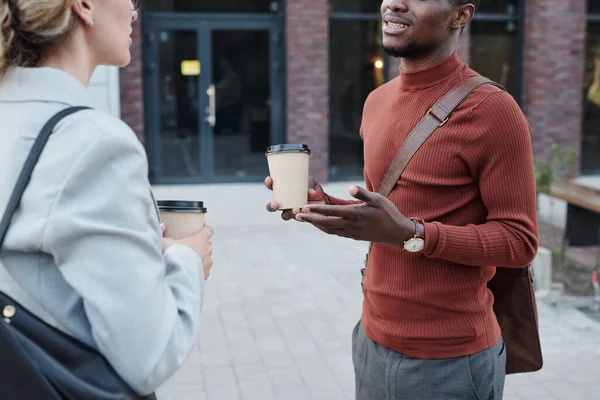 African man and Caucasian woman with drinks talking in the street