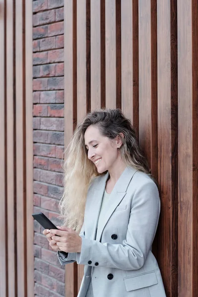 Glad ung kvinna i kostym SMS i smartphone — Stockfoto