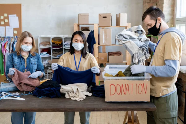 Mensen met maskers en handschoenen die donatiekleding kiezen — Stockfoto