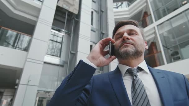 现代办公大楼内穿着蓝色西服的自信成熟商人或倡导者的低角度中慢镜头打电话 — 图库视频影像