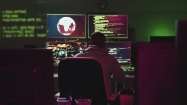 Arka planda tanınmayan bir adamın karanlık bir ofiste bilgisayar monitörlerinin önünde oturup önemli bilgilere erişimini hacklediği görüntüler var.