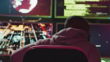 Tanımlanamayan şüpheli kapüşonlu bir adam bilgisayar monitörlerinin önünde oturuyor. Şifrelerini kırıyor, kaput takıyor ve kötü amaçlı yazılım üzerinde çalışmaya devam ediyor.