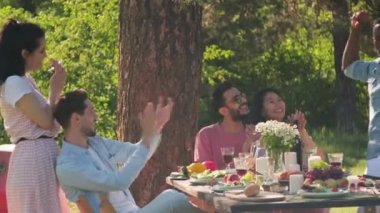 Bir grup modern, neşeli, çoklu etnik erkek ve kadın parkta eğleniyor, öğle yemeği yiyor, güneşli bir günde müzik dinliyor ve dans ediyor.