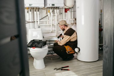 Üniformalı genç tamirci borunun bir kısmını inceliyor.