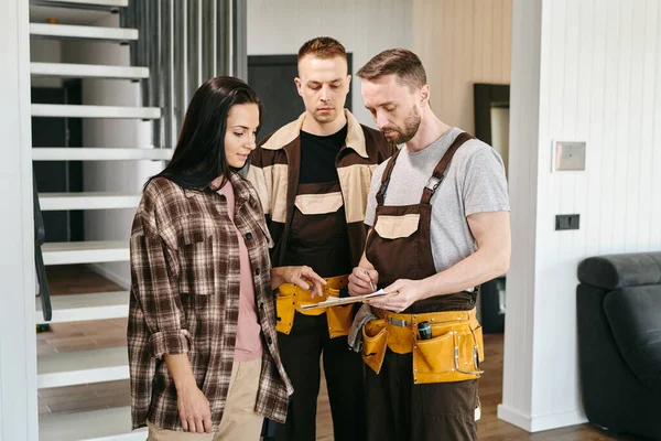 Zwei Klempner zeigen junger Frau, wo sie ihre Unterschrift setzen muss — Stockfoto