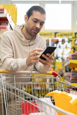 Akıllı telefonu ve alışveriş arabası olan bir erkek tüketici
