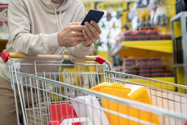 Ruce mužského zákazníka s chytrým telefonem a nákupním vozíkem — Stock fotografie