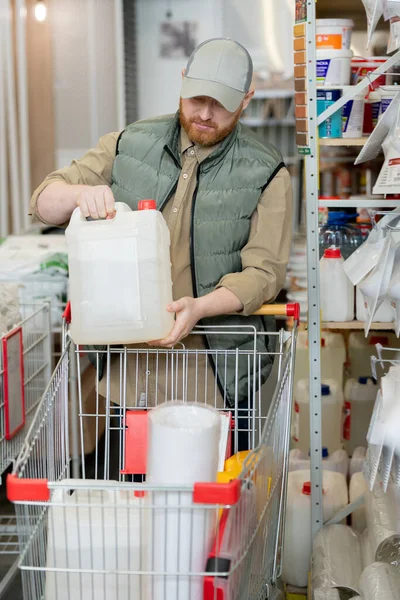 Současný muž dává plastovou nádrž do nákupního košíku — Stock fotografie