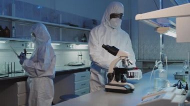 Tek kullanımlık tulumlar, gözlükler, eldivenler ve maske takan ve kan örnekleriyle dolu test tüpleri taşıyan siyah erkek epidemiyolojistin yavaş çekimleri.