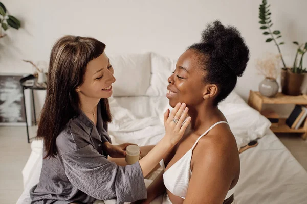 Jovem feliz aplicando creme facial no rosto de sua namorada — Fotografia de Stock