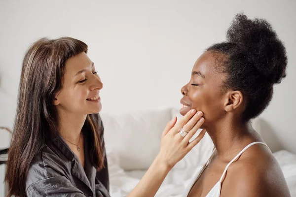 Mulher feliz aplicando creme no rosto de sua namorada africana — Fotografia de Stock