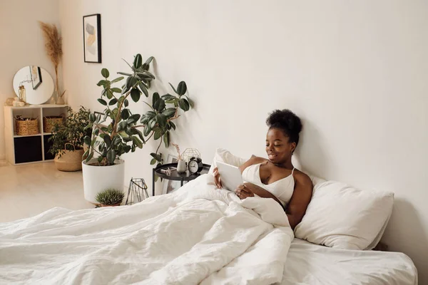 Junge Afrikanerin mit Tablette im Bett — Stockfoto