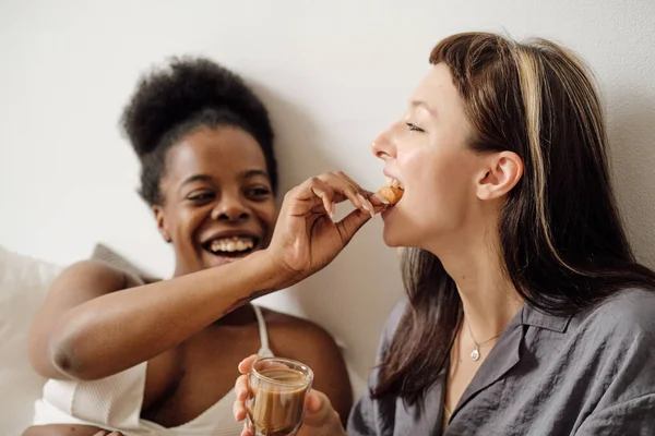 Heureuse femme africaine mettant morceau de croissant dans la bouche de sa petite amie — Photo