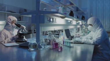 Yüz maskeli ve koruyucu tulumlu çeşitli epidemiyoloji gruplarından oluşan yavaş PAN laboratuvarda araştırma yapıyor.