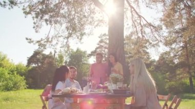 Çok ırklı erkek ve kadınların dışarıda dışarıda yemek yiyip sohbet ederek harika vakit geçirdikleri geniş açılı görüntüler.