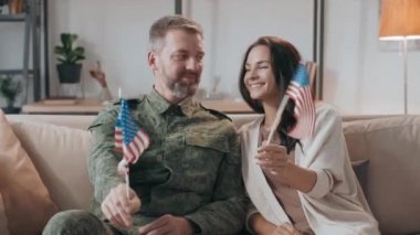 Askeri üniformalı mutlu orta yaşlı erkek subayın portre resmi ve onun neşeli karısı koltukta oturmuş kameraya bakarken Amerikan bayraklarını sallıyor.