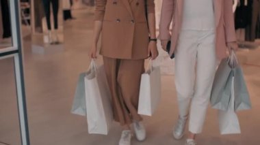 Alışveriş merkezinden alışveriş torbaları taşıyan, alışveriş merkezinden çıkan ve sohbet eden mutlu genç bayanlarla yavaş takip.