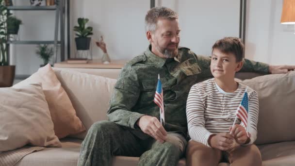 身着军服的中年男军官和他的儿子坐在沙发上举着美国国旗的画像 — 图库视频影像