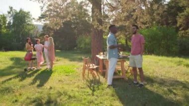 Çok ırklı genç erkek ve kadın grupları günü yerel parktaki barbekü partisinde geçiriyorlar.