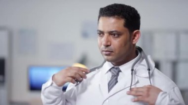 Orta boy, Orta Doğulu bir doktorun beyaz önlük giyip boynuna steteskop taktığı portre görüntüleri.