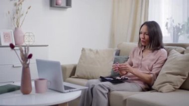 İnternetteki tıbbi konsültasyon sırasında kanındaki glikoz seviyesini ölçen olgun bir kadın dizüstü bilgisayarın önünde oturuyor.