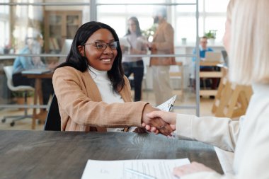 Neşeli Afrikalı kadın uzman iş görüşmesinden sonra yeni işverenin elini sıkıyor.