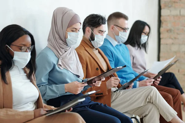 Personnes multiraciales avec des masques de protection assis le long du mur dans le couloir — Photo