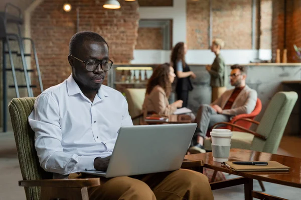 Young African businessman with laptop networking against colleagues — Stock Photo, Image