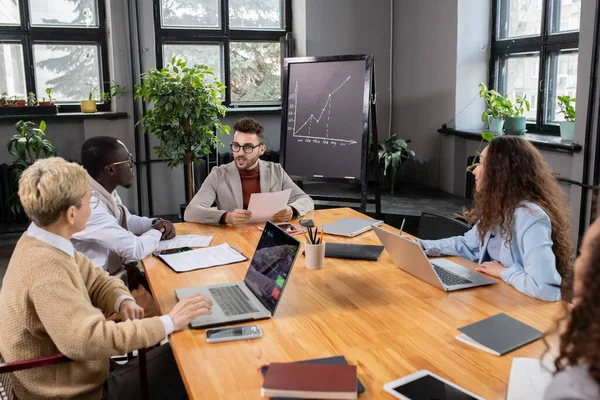 Entrenador con el papel sentado por la mesa delante de los gerentes — Foto de Stock