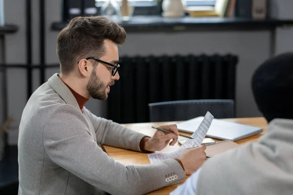 Male speaker pointing at paper while looking through data — Stock Photo, Image