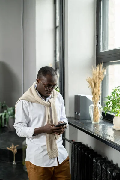 Jovem empresário africano rolando no smartphone no escritório — Fotografia de Stock