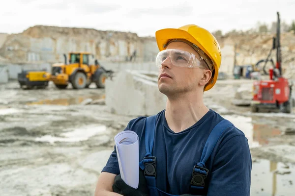 Ung gruvarbetare i hatt och glasögon tittar på husbyggnad — Stockfoto