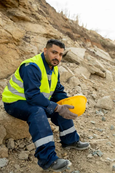 Young mixed-race builder sitting by construction site and having rest — Stock Photo, Image