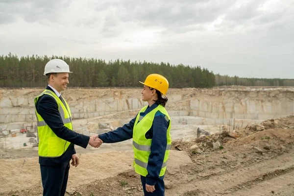 Två kollegor i hardhattar och arbetskläder skakar hand — Stockfoto