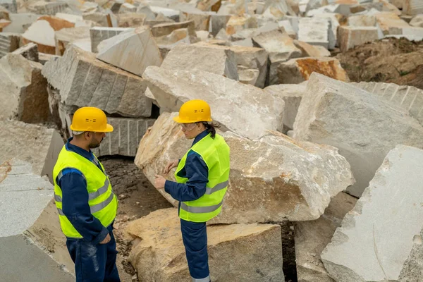 Dos constructores contemporáneos en ropa de trabajo interactuando entre enormes bloques — Foto de Stock