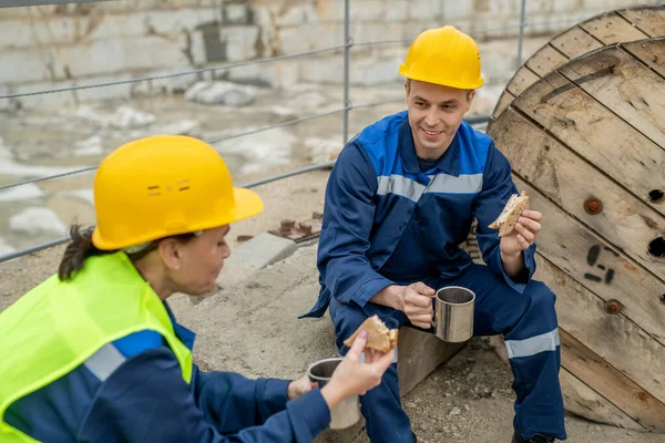 Dos constructores en sombreros y ropa de trabajo que tienen sándwiches con té —  Fotos de Stock