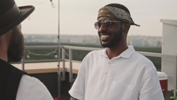アフリカ系アメリカ人と白人の男性のスローモハンドヘルド追跡笑顔とチャットパーティーで屋上テラス — ストック動画
