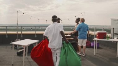 Fasulye torbaları taşıyan, çatıdaki partiye gelen, sonra arkadaşlarına sarılan ve ellerini sıkan Afro-Amerikan bir adamın el kamerası görüntüsü.