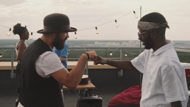 幸せな白人男性と彼のアフリカ系アメリカ人の友人は 屋上パーティーで拳バンプでお互いに挨拶し その後チャット — ストック動画