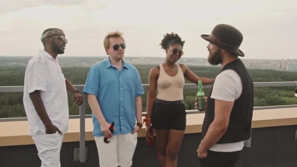 アフリカ系アメリカ人と白人の友人がビールボトルを持っていて 屋上のテラスでチャットしている様子をスローモーションで追跡 — ストック動画