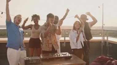 Genç bir kadın çatıdaki partide mikrofona şarkı söylerken, el kamerasıyla mutlu erkek DJ 'in seti. Gençler güzel bir yaz akşamı terasta bira içip dans ediyorlar.