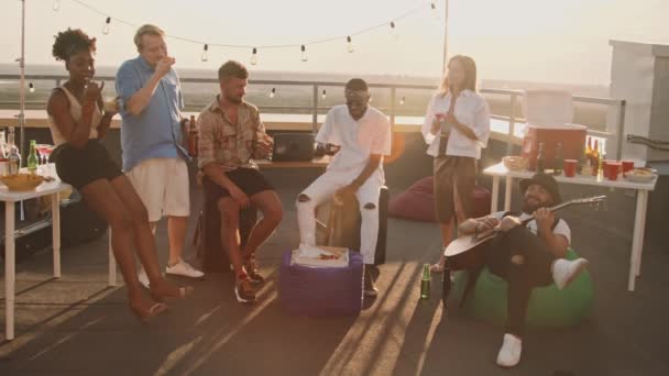 お酒を楽しみながら 素敵な夏の夜に屋上テラスで過ごす多様な若者たちの手によるスロモ — ストック動画
