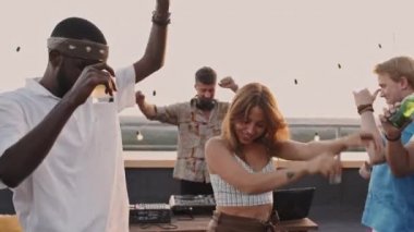 DJ güzel bir yaz akşamında seti çalarken çatıdaki terasta gülen ve dans eden genç erkek ve kadınların orta boy fotoğrafları.