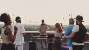 El bilgisayarı takibi, neşeli sakallı erkek DJ seti çalarken güzel bir yaz akşamı terasta dans eden mutlu gençleri çekiyor.