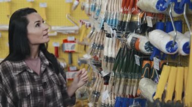 Hırdavatçıdaki raflara doğru yürüyen ve boya fırçasını seçen güzel bir genç kadının yavaş çekimleri.