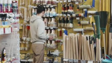 Alışveriş çantalı genç adamın boya fırçası ve boya silindirini seçerken ki yavaş çekimi.