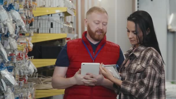 在五金店 穿着肥大背心的男性员工慢镜头帮助年轻女性顾客选择用品 — 图库视频影像