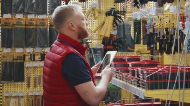 Erkek hırdavatçı amirinin raflardaki ürünleri kontrol ederken ve tablet üzerinde yazarken elde çekilen yavaş çekimi