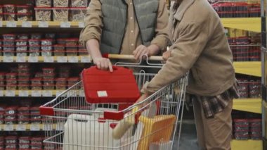 Bir çiftin alışveriş arabasına erzak koyarken ve ev dekorasyonu mağazasında kameraya poz verirken yavaş çekimde.