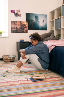 Sorunlu kız yerde oturuyor ve bacaklarını kucaklıyor.